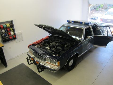 1991 Ford LTD Crown Victoria - A police car sits in a garage with its hood and driver's door open, revealing the engine compartment.