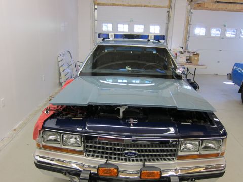 1991 Ford LTD Crown Victoria - Front view of a dark blue Ford Crown Victoria police car with its hood up, parked inside a garage.