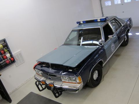 1991 Ford LTD Crown Victoria - A dark blue and light blue police car is parked inside a garage with its hood up.