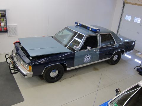 1991 Ford LTD Crown Victoria - A two-tone blue and gray police car sits in a garage with its hood open and a light bar on the roof.