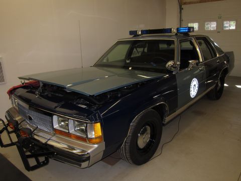 1991 Ford LTD Crown Victoria - A 1991 Ford Crown Victoria LTD police car is shown with its hood open, parked indoors with a light bar on the roof.