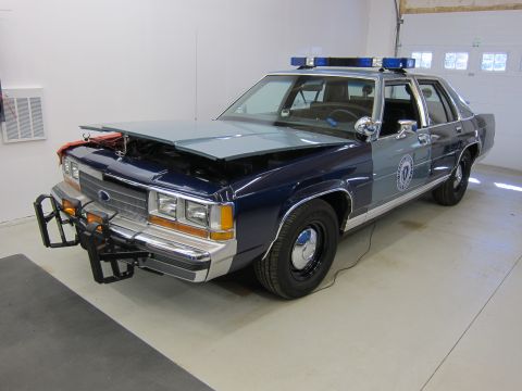 1991 Ford LTD Crown Victoria - A two-tone blue and gray police car is parked inside a garage with its hood up, revealing the engine compartment.
