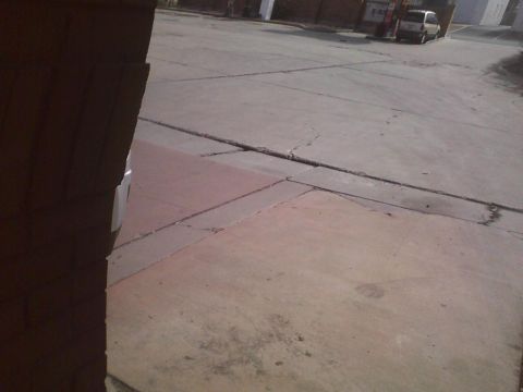 2003 Ford Crown Victoria - A street scene shows a parked van and a brick structure, with cracked pavement in the foreground.