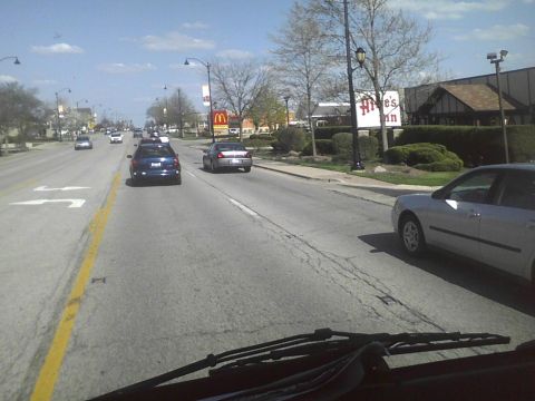 2003 Ford Crown Victoria - A silver sedan is seen from the driver's perspective on a road with multiple vehicles and commercial buildings.