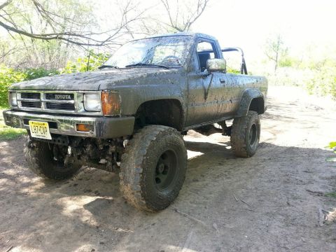 1987 Toyota 4Runner - Muddy 1987 Toyota pickup truck with off-road tires in a wooded area.