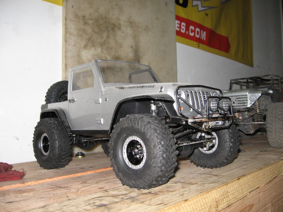Silver RC Jeep Wrangler with large tires and off-road bumper, parked on a wooden surface