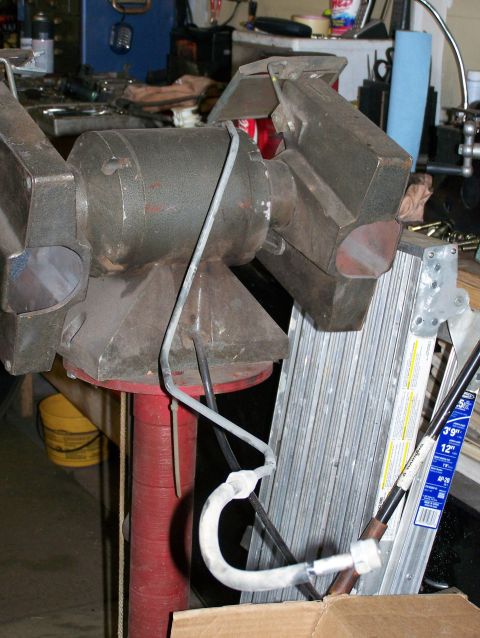 1988 Suzuki Samurai - A large vise is mounted on a red stand, holding a bent metal tube.