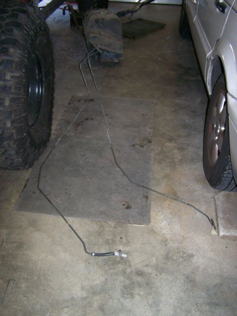 1988 Suzuki Samurai - Fuel lines are visible on the garage floor, near a large tire and vehicle frame components.