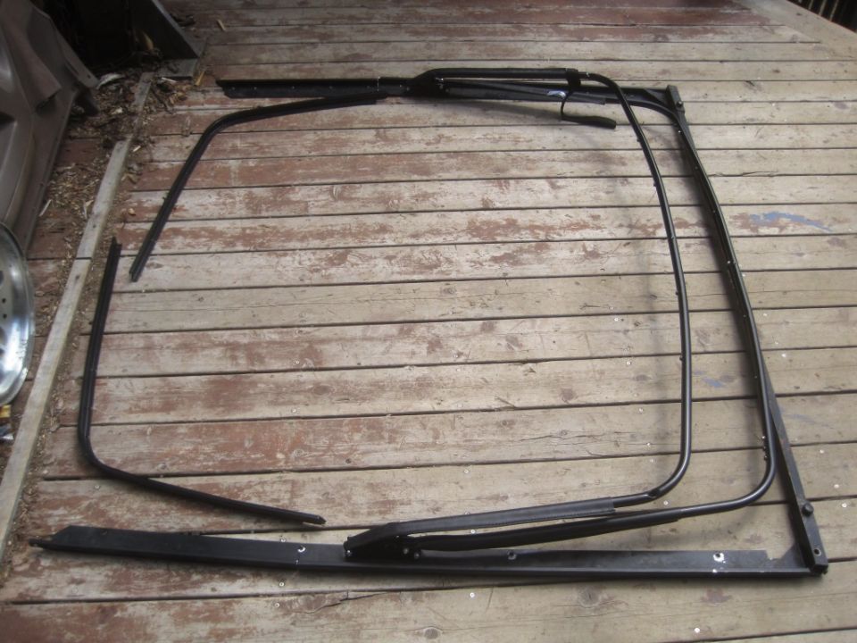 Soft top frame pieces laid out on a wooden deck. Includes curved metal bars and a long flat section