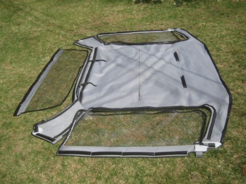 1993 Ford Bronco - A gray soft top with clear windows is displayed on a grassy surface, likely a replacement part for a vehicle.