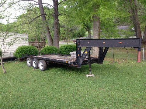 1989 Ford Bronco - A black gooseneck trailer with triple axles sits on a lawn in front of trees and a house.