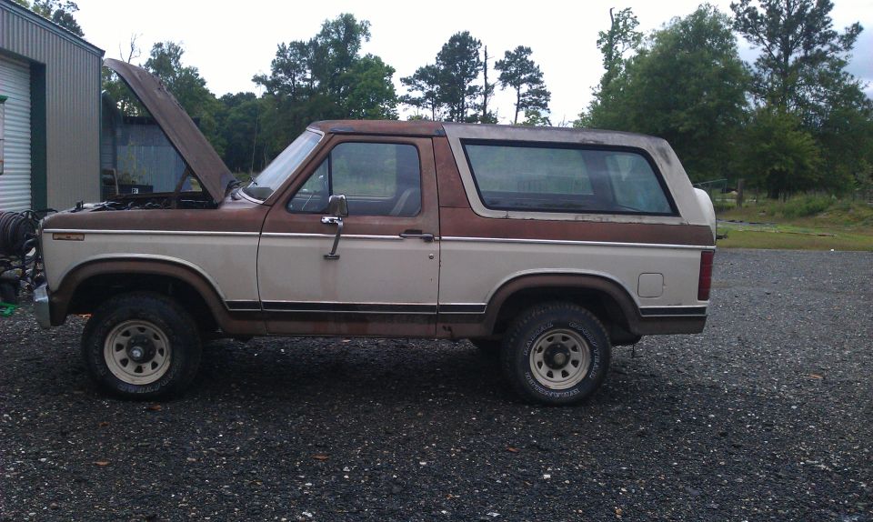 Brown and tan Ford Bronco with hood open, parked on gravel