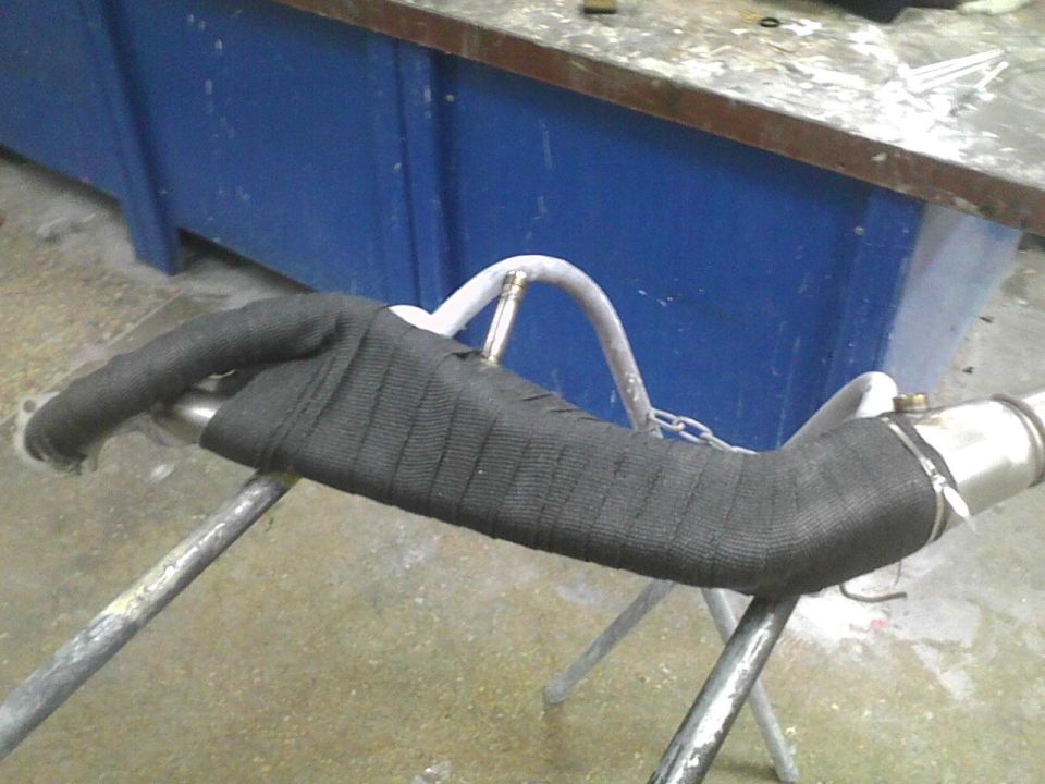 Exhaust pipe section wrapped in black heat tape, supported by metal stands