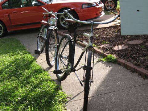 1994 Ford Bronco - Two bicycles are parked on a concrete sidewalk next to a red car.