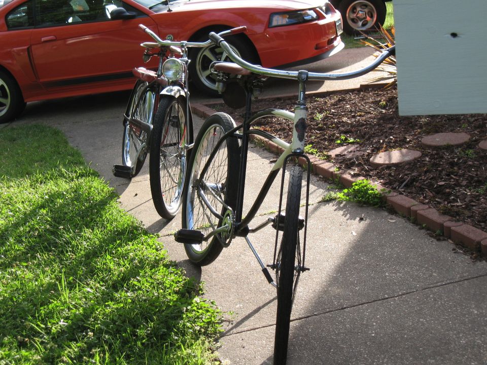 Two bicycles parked on a sidewalk in front of a red car