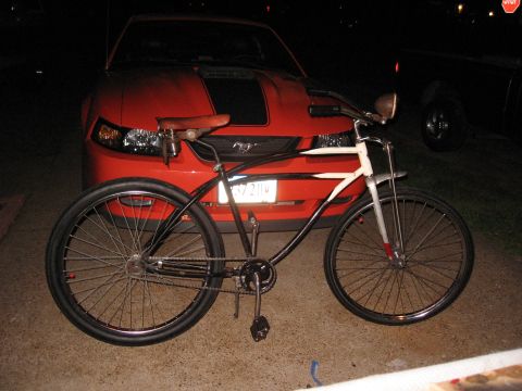 1994 Ford Bronco - A vintage bicycle is positioned before a red Ford Mustang at night.