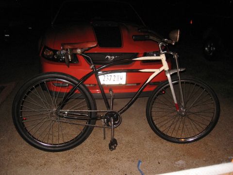 1994 Ford Bronco - A vintage-style bicycle is parked in front of a red car at night.