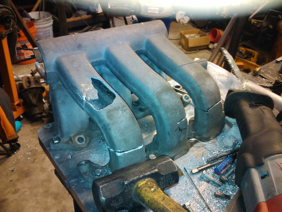 Damaged aluminum intake manifold with broken runners and tool marks, on a workbench