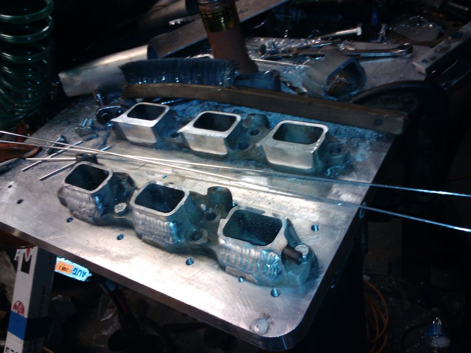 Engine intake manifold with four ports on a metal surface, with a brush and metal rods
