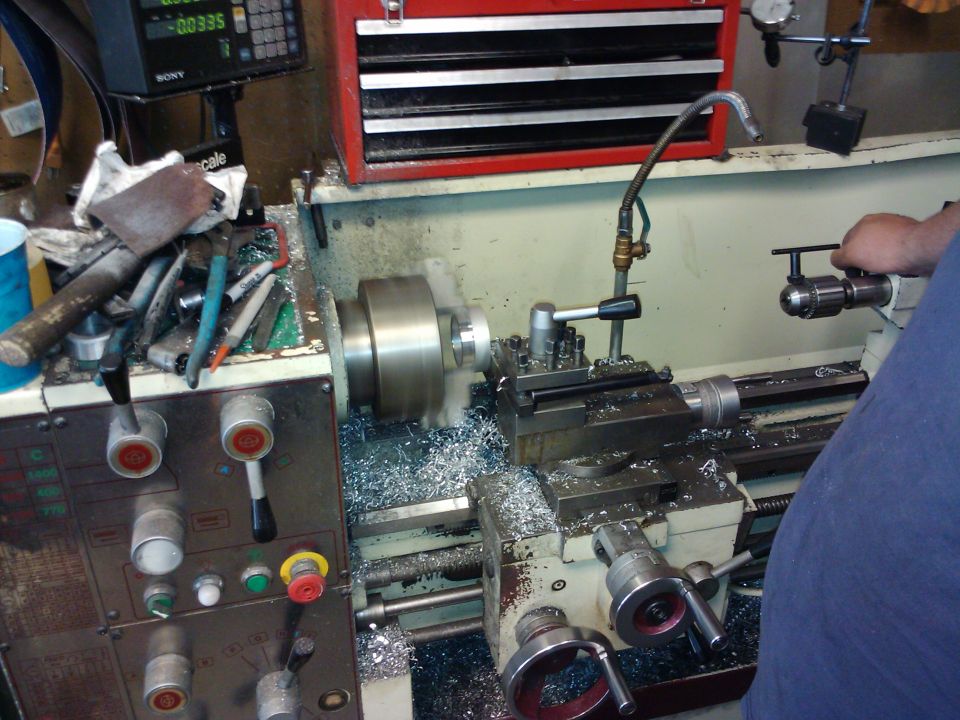 Lathe cutting metal, shavings everywhere. Someone's hand is on the drill chuck