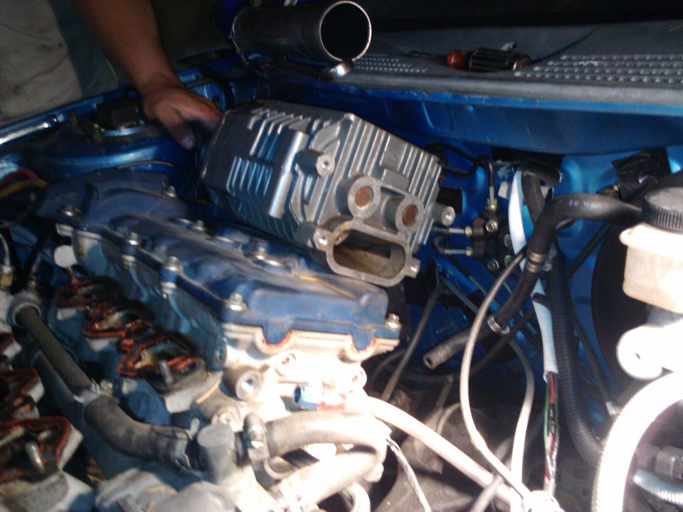 Supercharger being installed onto a blue engine block with various hoses and wires visible