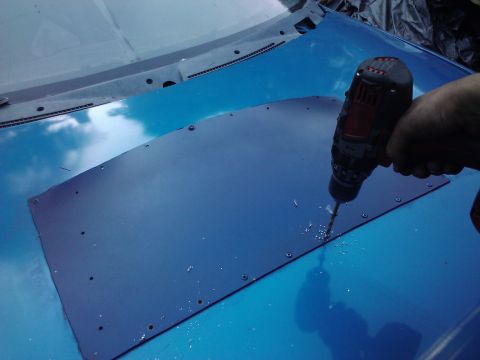 1995 Ford Probe - A person drills holes into a dark panel being installed on the hood of a blue car.