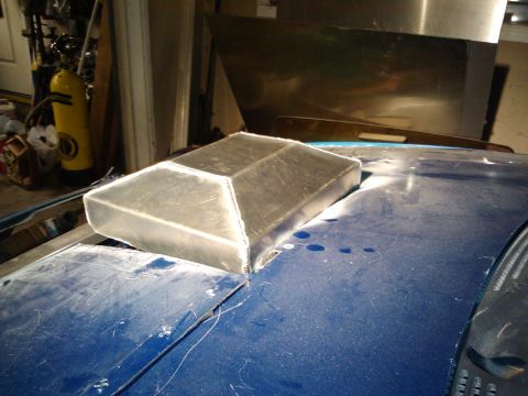 1995 Ford Probe - A custom aluminum hood scoop is being fitted onto a blue car's hood in a garage setting.