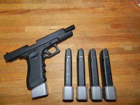 1996 Ford Bronco - A black pistol with an extended magazine sits next to four spare magazines on a wooden surface.