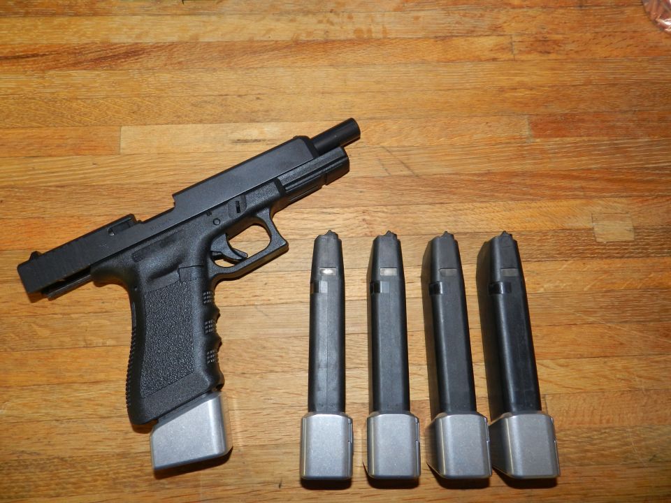 Black pistol with extended magazine and four spare magazines on a wooden surface