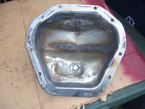 1968 Ford Bronco - A metal differential cover, showing signs of welding and a central drain plug, is placed on a cardboard surface.
