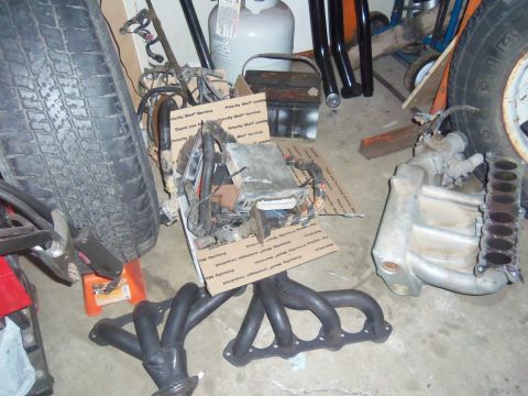 1968 Ford Bronco - Various engine components are laid out on the floor of a garage, including a manifold and exhaust headers.