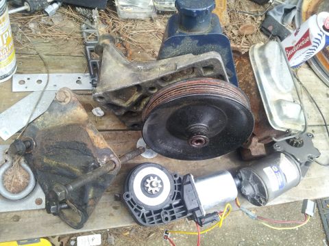 1986 Ford Bronco - A collection of automotive components, including a power steering pump and motors, are displayed on a weathered wooden surface.