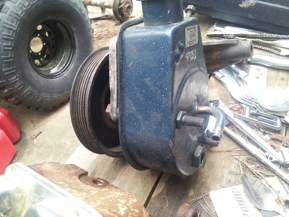 Blue power steering pump with pulley, next to a tire and axle assembly