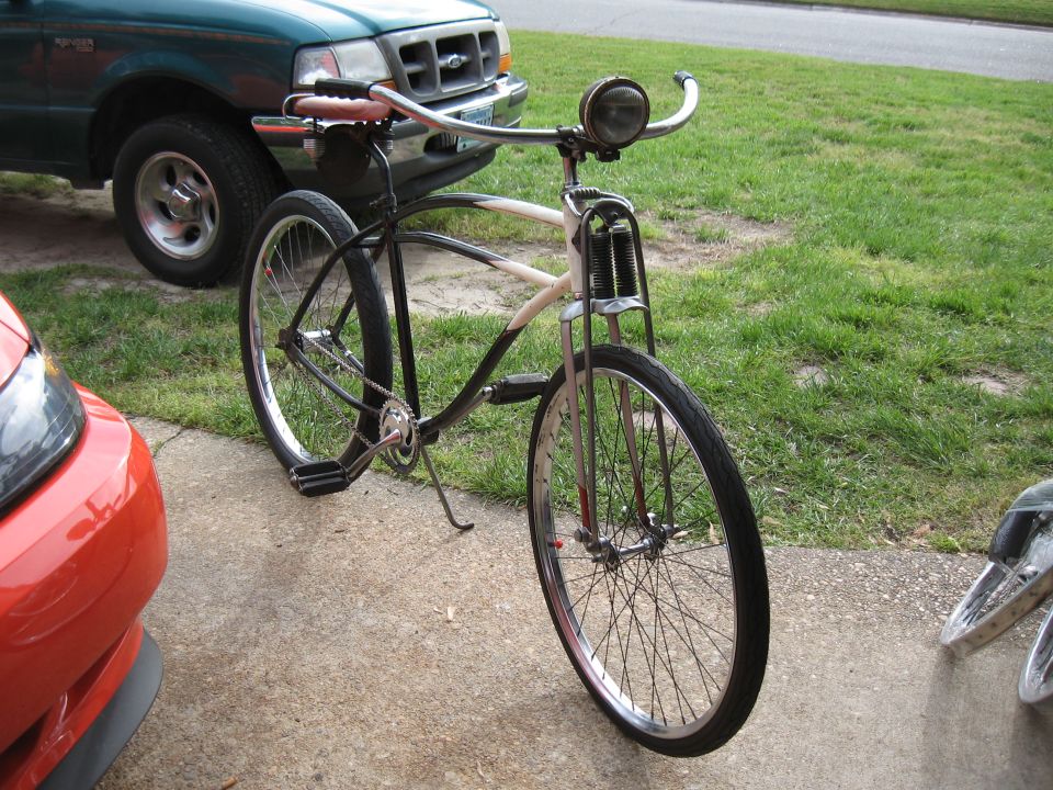 Front view of a vintage bicycle with a green truck and red car in the background