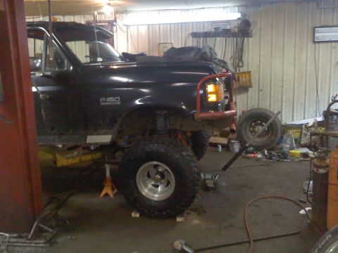 1995 Ford F-150 - A black 1995 Ford F-150 truck is shown in a garage, lifted on jack stands with a red bull bar attached.