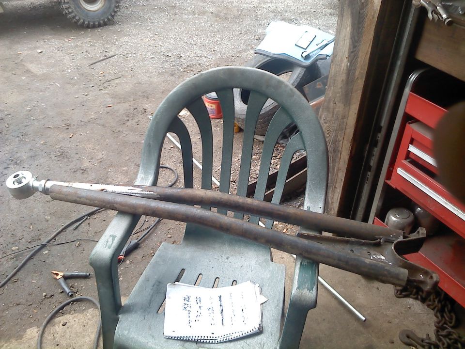 Pair of rusty suspension control arms resting on a green plastic chair. A notebook lies on the seat