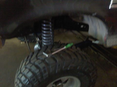 1995 Ford F-150 - A tool rests on a large tire next to a suspension coil, indicating work on a vehicle's undercarriage.