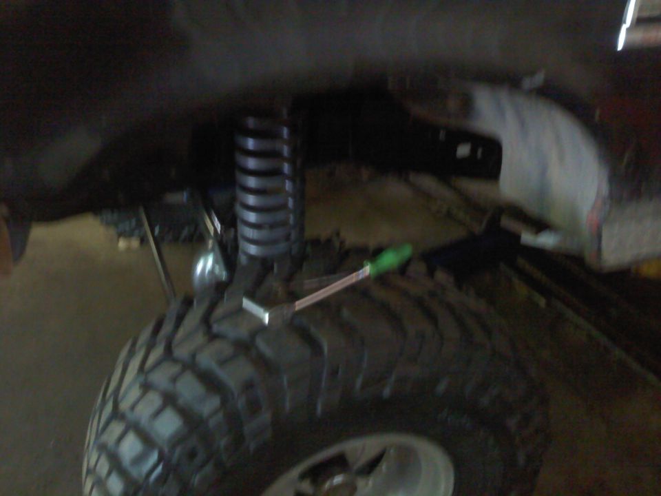 Close-up of a large off-road tire and suspension coil with a tool resting on the tire