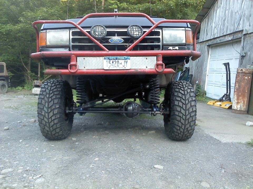 Front view of a lifted Ford truck with a red bull bar and large off-road tires. New York license plate 15420-JY is visible