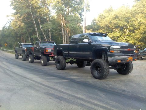 1995 Ford F-150 - Multiple heavily modified pickup trucks are parked in a line on a road.
