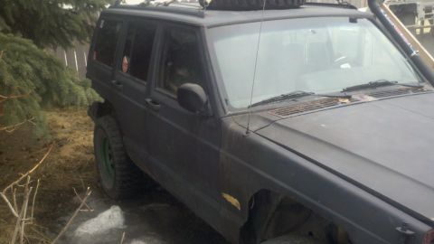 1998 Jeep Cherokee - A dark-colored Jeep Cherokee is parked outdoors, showing its front-right side with a snorkel and roof rack.