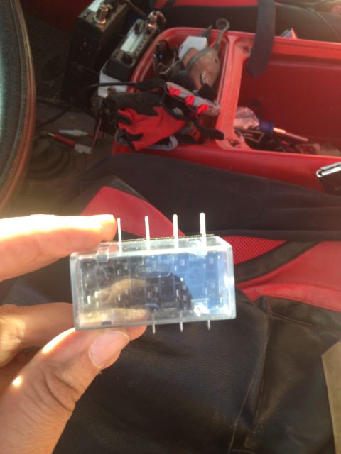 1979 Ford Bronco - A clear relay with metal pins is held in front of a vehicle's red interior and black seat.