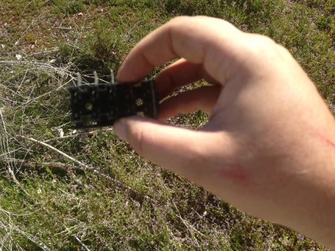 1979 Ford Bronco - A hand holds a small black electronic component outdoors against a backdrop of dry vegetation.