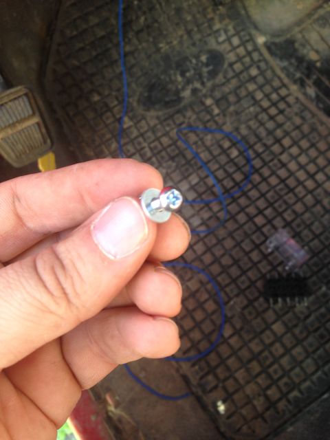 1979 Ford Bronco - A hand holds a screw with a blue wire, against a textured floor mat.