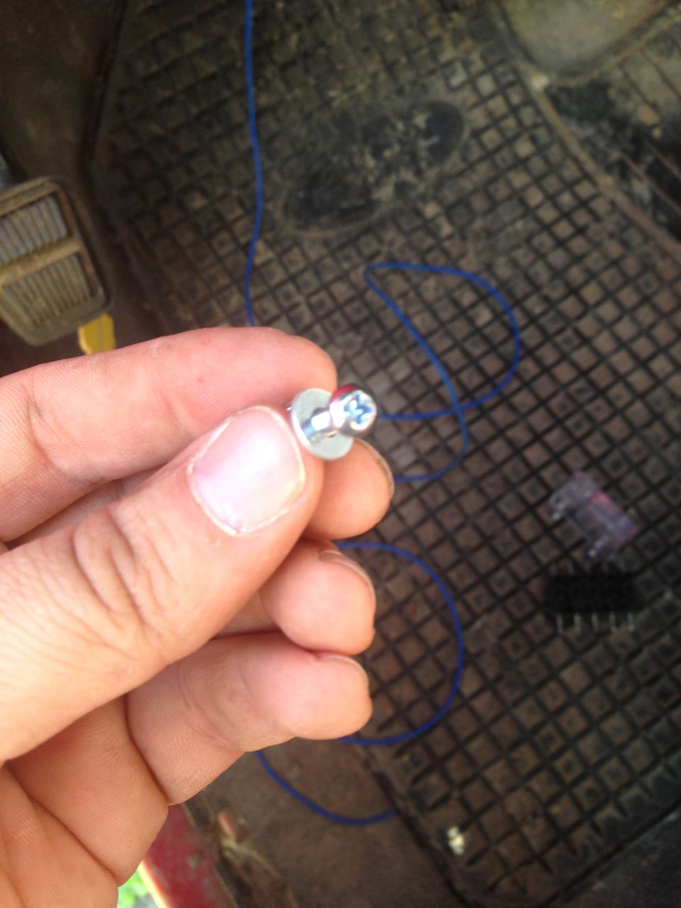 Hand holding a screw with blue wire on a black floor mat