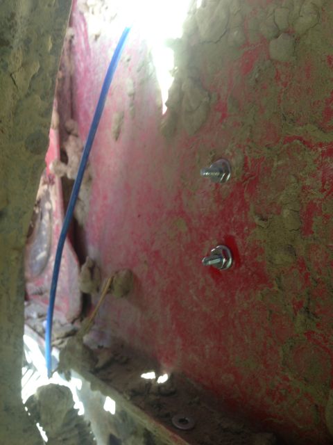 1979 Ford Bronco - Close-up view of a dirty red panel with visible bolts and a blue wire, likely a vehicle part.