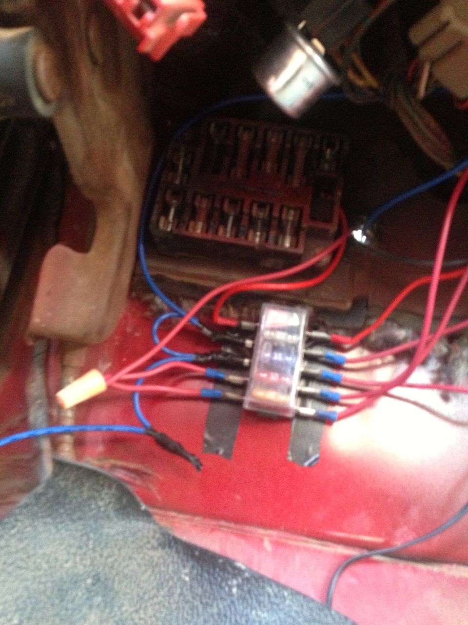 Red metal surface with a fuse box, inline fuse holder, and red and blue wires