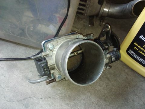 1995 Ford Probe - A car part, a throttle body, is shown with a yellow fluid container in the background.