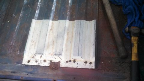 1979 Ford Bronco - A close-up view of a corrugated metal panel on a rusty surface, with tools visible to the right.