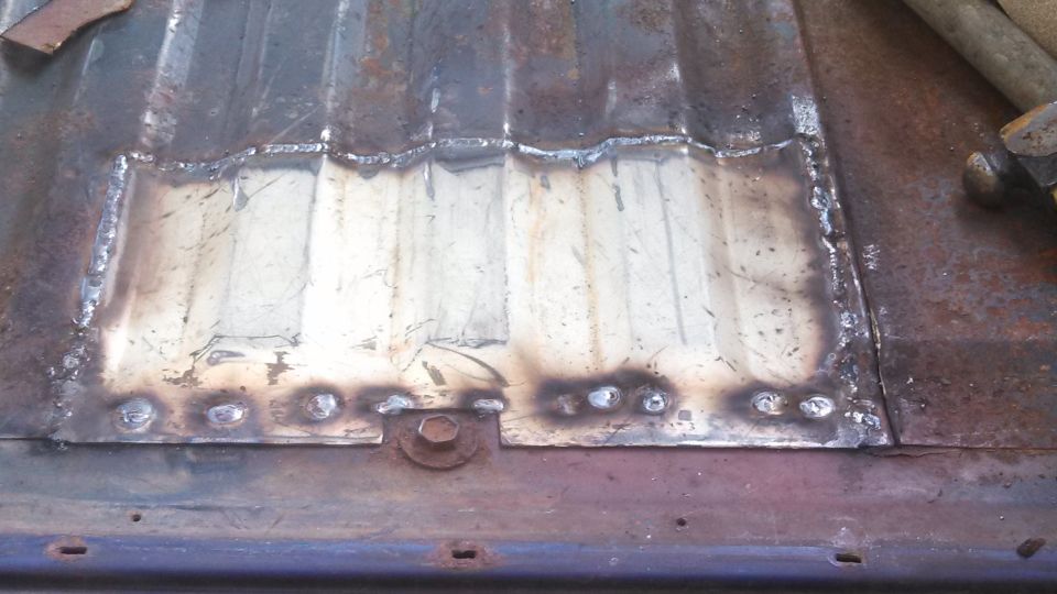 Corrugated metal surface with a welded patch and a bolt